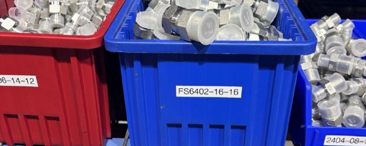 Bins of staged fittings labeled by part number